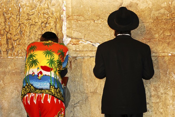 An Orthodox Jewish man and a tourist stand side by side at the Western (Wailing) Wall praying fervently.