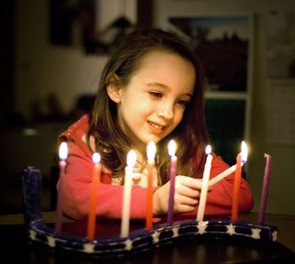A young Jewish girl admires the light of the fully lit Chanukah menorah.