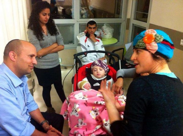 Naftali Bennet speaks with Adva Biton. while young Adele rests in a stroller.