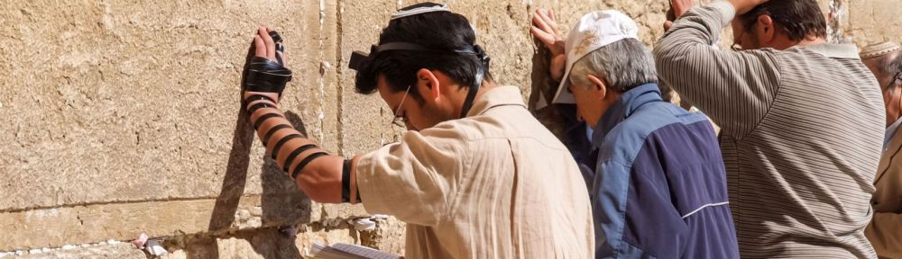 Siddur-Jewish prayer at the Western (Wailing) Wall in Jerusalem. The man wearing tefillin (phylacteries) is reading from a Siddur.