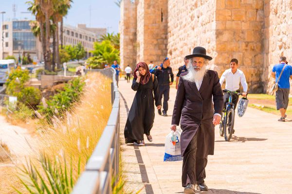 An elderly orthodox Jewish man walks with other Israelis and tourists  outside the Old City walls of Jerusalem.