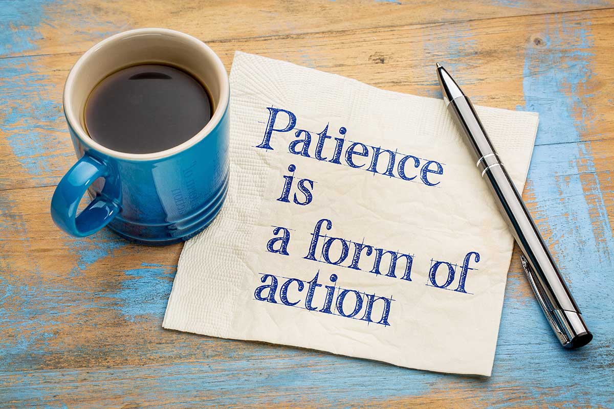 The words "patience is a form of action" are written on a piece of paper with a cup of coffee and a pen on a table.